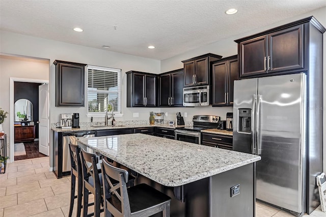 kitchen featuring sink, a textured ceiling, appliances with stainless steel finishes, a kitchen island, and a kitchen bar