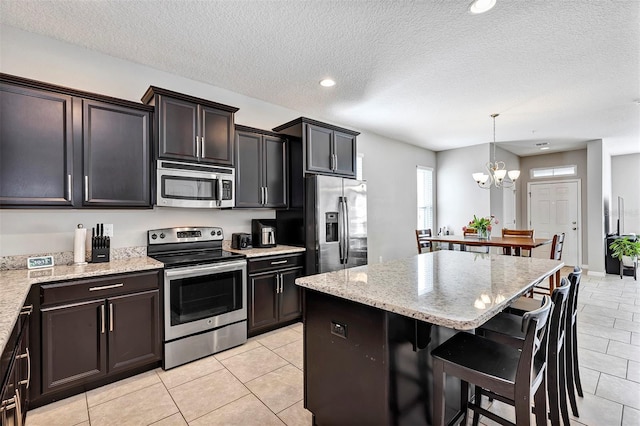 kitchen with stainless steel appliances, an inviting chandelier, a textured ceiling, decorative light fixtures, and a kitchen island