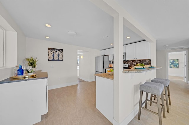 kitchen featuring backsplash, white refrigerator, kitchen peninsula, light stone countertops, and white cabinetry