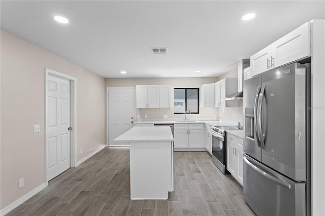 kitchen featuring wall chimney range hood, a kitchen island, range hood, white cabinets, and appliances with stainless steel finishes