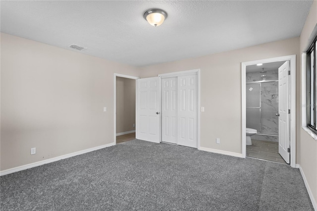 unfurnished bedroom featuring connected bathroom, a closet, a textured ceiling, and dark colored carpet