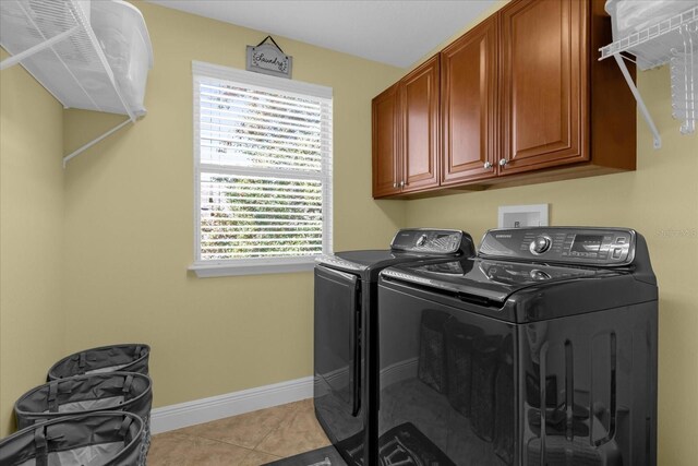 clothes washing area featuring washer and clothes dryer, cabinets, and light tile patterned floors