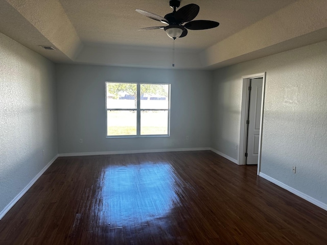 empty room with a raised ceiling, ceiling fan, dark hardwood / wood-style flooring, and a textured ceiling