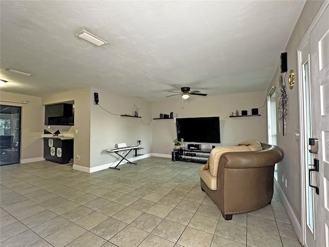 living room with ceiling fan, light tile patterned flooring, and a textured ceiling