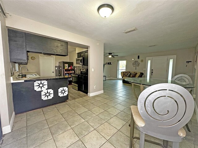 interior space with appliances with stainless steel finishes, a textured ceiling, ceiling fan, sink, and light tile patterned floors