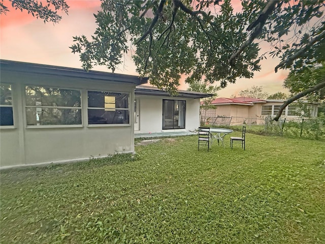 back house at dusk featuring a lawn