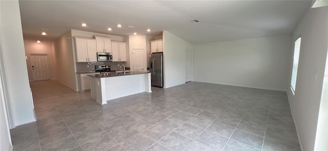 kitchen with light tile patterned floors, backsplash, an island with sink, white cabinets, and appliances with stainless steel finishes