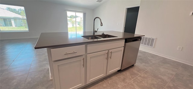 kitchen with stainless steel dishwasher, sink, white cabinets, an island with sink, and light tile patterned flooring