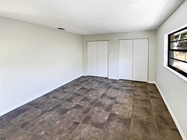 unfurnished bedroom featuring a textured ceiling and two closets