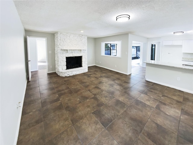 unfurnished living room with a stone fireplace and a textured ceiling