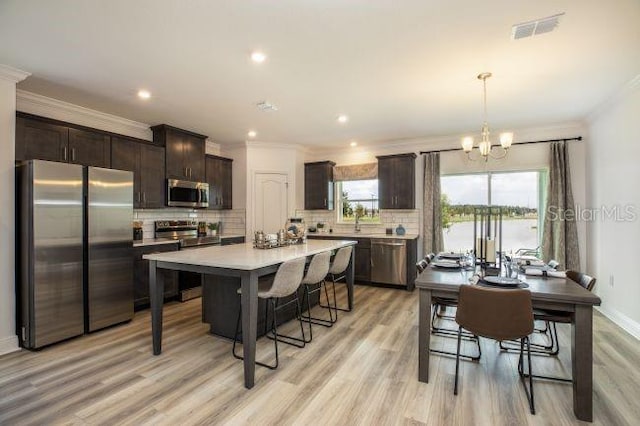 kitchen with decorative light fixtures, crown molding, appliances with stainless steel finishes, and light hardwood / wood-style flooring