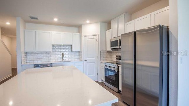 kitchen with sink, tasteful backsplash, wood-type flooring, white cabinets, and appliances with stainless steel finishes