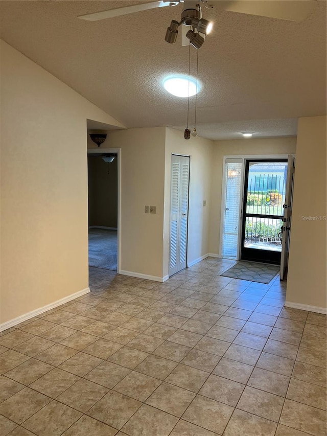 tiled spare room with ceiling fan, vaulted ceiling, and a textured ceiling