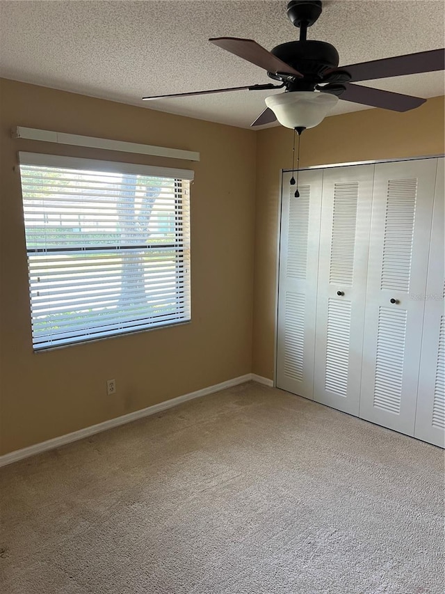 unfurnished bedroom with ceiling fan, carpet flooring, a textured ceiling, and a closet