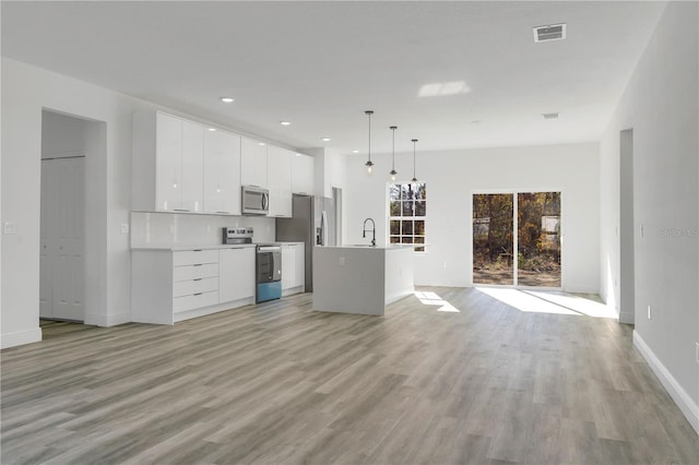 kitchen with stainless steel appliances, a kitchen island with sink, decorative light fixtures, light hardwood / wood-style flooring, and white cabinetry