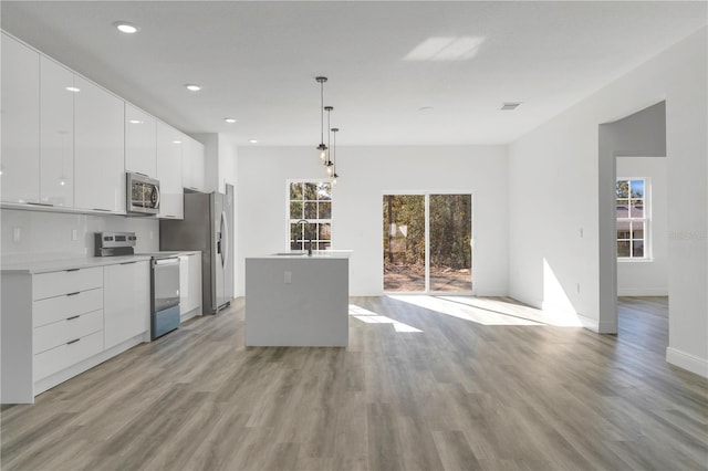 kitchen featuring light wood-type flooring, stainless steel appliances, sink, pendant lighting, and white cabinetry