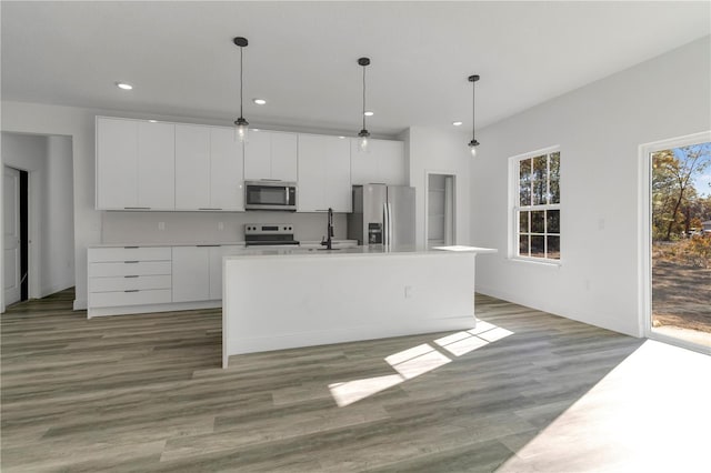 kitchen with a kitchen island with sink, white cabinets, sink, decorative light fixtures, and stainless steel appliances