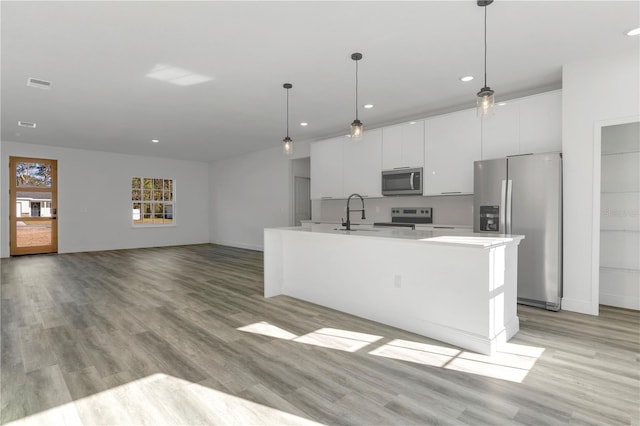 kitchen featuring stainless steel appliances, a center island with sink, light hardwood / wood-style flooring, white cabinetry, and hanging light fixtures