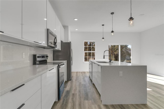 kitchen featuring a kitchen island with sink, sink, hanging light fixtures, appliances with stainless steel finishes, and white cabinetry