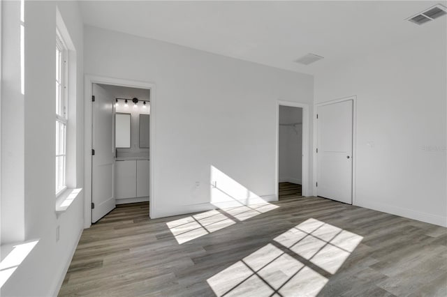 unfurnished bedroom featuring a walk in closet, light hardwood / wood-style flooring, connected bathroom, and a closet