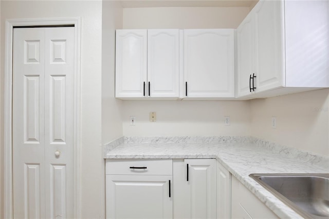 kitchen featuring white cabinets, light stone countertops, and sink