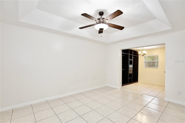 spare room featuring a raised ceiling, light tile patterned floors, ceiling fan with notable chandelier, and a textured ceiling