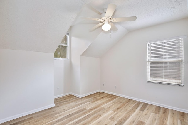 additional living space with a textured ceiling, a wealth of natural light, vaulted ceiling, and light wood-type flooring