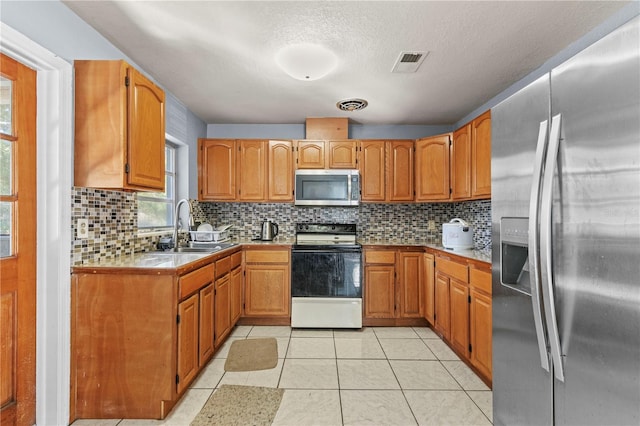 kitchen featuring sink, a textured ceiling, tasteful backsplash, light tile patterned flooring, and stainless steel appliances