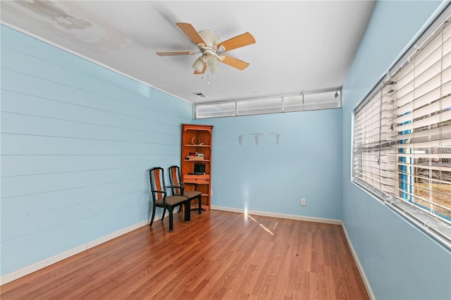 sitting room with ceiling fan, hardwood / wood-style floors, and wooden walls