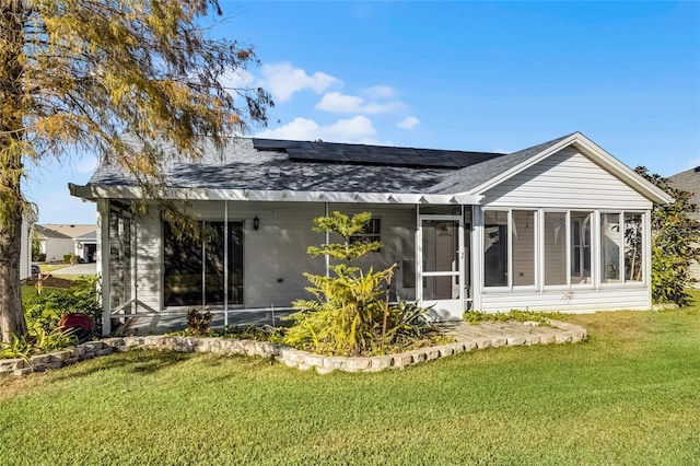 rear view of house featuring a lawn, a sunroom, and solar panels