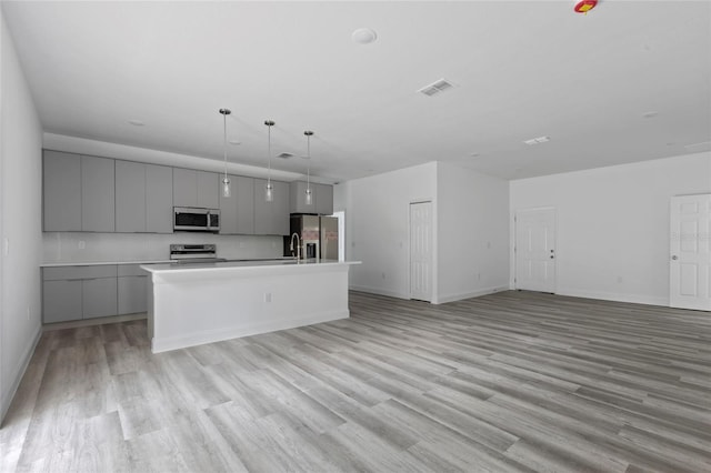 kitchen with stainless steel appliances, gray cabinets, a kitchen island with sink, and light hardwood / wood-style floors