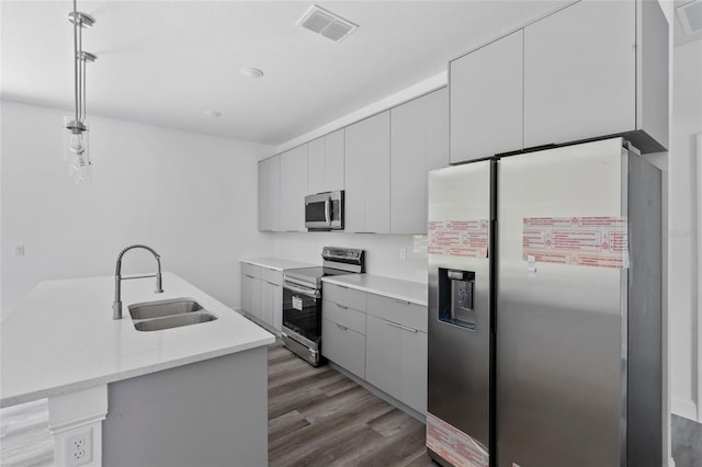 kitchen featuring sink, wood-type flooring, pendant lighting, gray cabinets, and appliances with stainless steel finishes