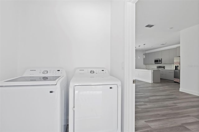 clothes washing area with separate washer and dryer, light hardwood / wood-style floors, and sink