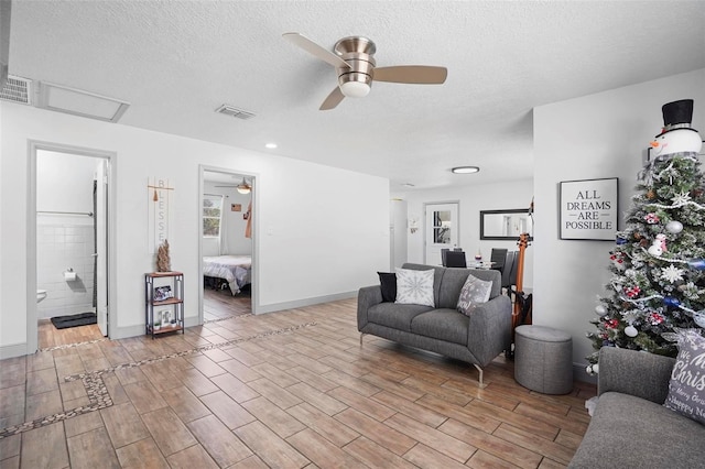 living room featuring ceiling fan, light hardwood / wood-style flooring, and a textured ceiling