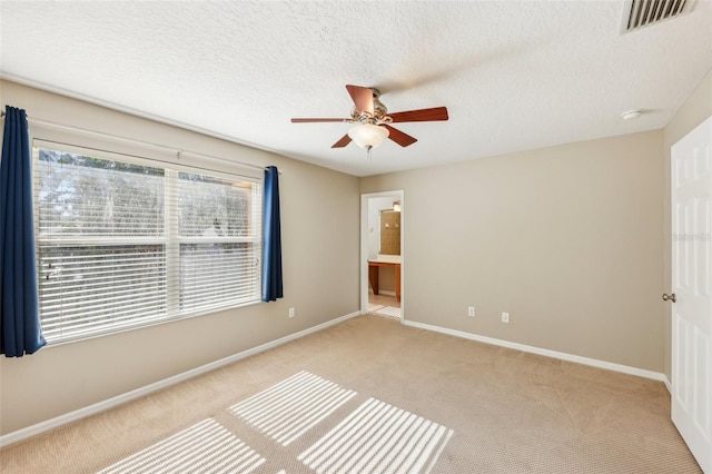 unfurnished bedroom with ensuite bathroom, ceiling fan, light carpet, and a textured ceiling