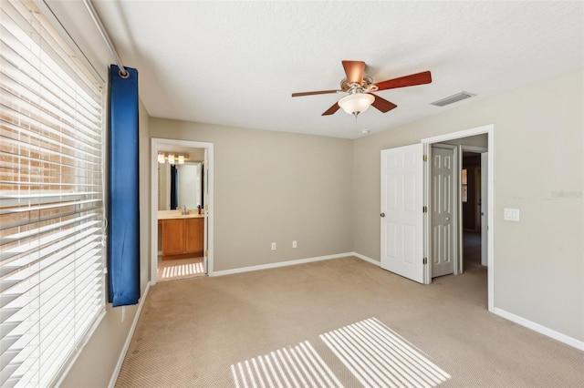 unfurnished bedroom with ensuite bathroom, ceiling fan, light carpet, and a textured ceiling