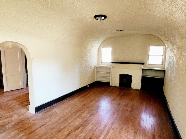 unfurnished living room with a textured ceiling, hardwood / wood-style flooring, and lofted ceiling