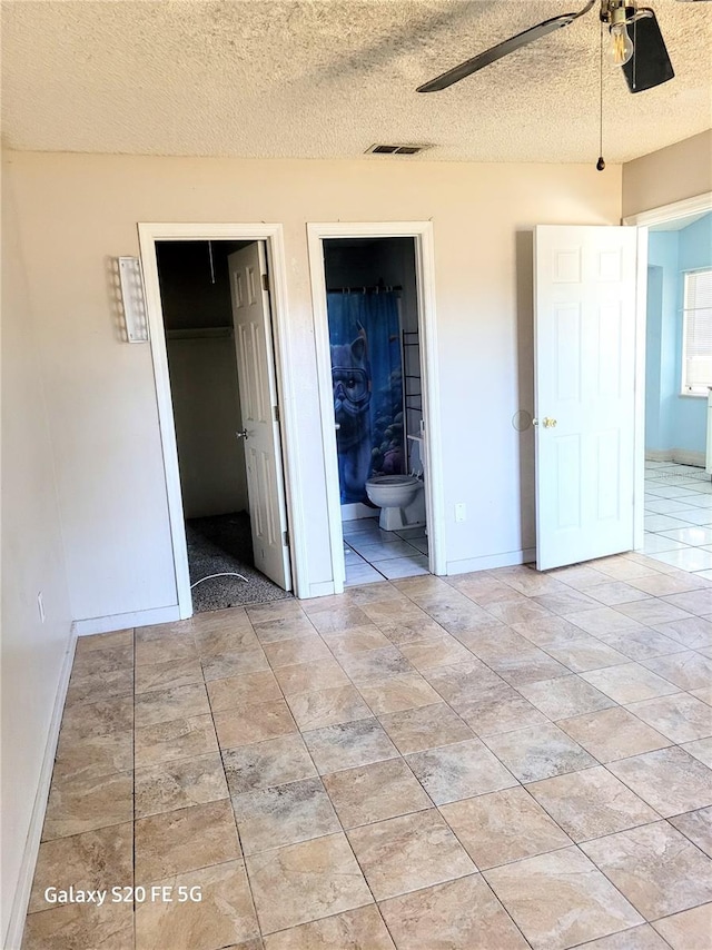 unfurnished bedroom with a walk in closet, ensuite bath, ceiling fan, a textured ceiling, and a closet