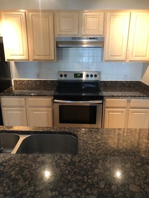 kitchen featuring dark stone countertops, stainless steel electric range oven, fridge, and decorative backsplash