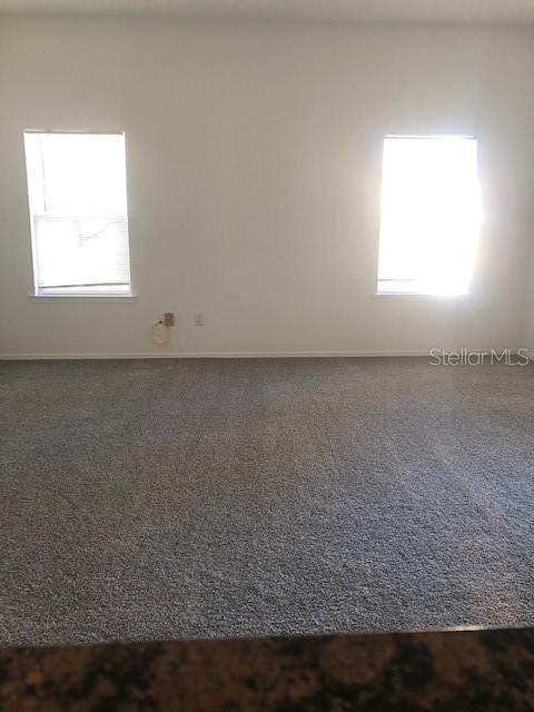 unfurnished room with dark colored carpet and a healthy amount of sunlight