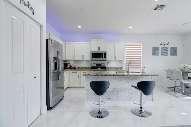 kitchen featuring dark stone counters, a center island with sink, a kitchen bar, white cabinetry, and stainless steel appliances