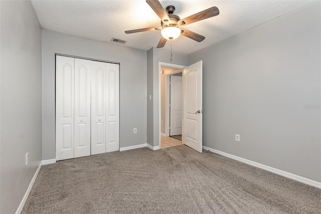 unfurnished bedroom featuring ceiling fan, light colored carpet, a textured ceiling, and a closet