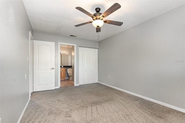 unfurnished bedroom with ceiling fan, ensuite bathroom, light colored carpet, a textured ceiling, and a closet