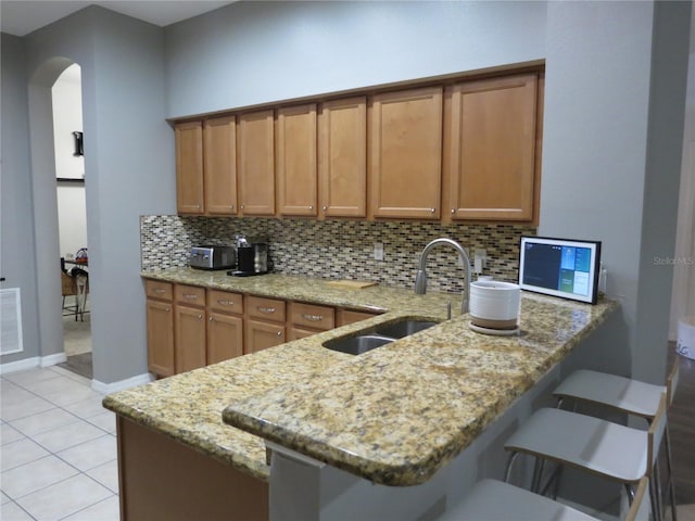 kitchen with sink, tasteful backsplash, light stone counters, kitchen peninsula, and a breakfast bar