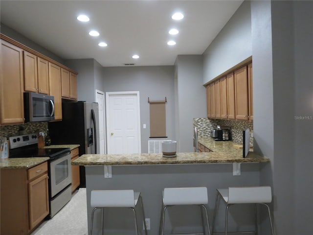 kitchen with stainless steel appliances, light stone counters, backsplash, kitchen peninsula, and a breakfast bar area