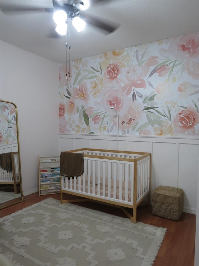 unfurnished bedroom with hardwood / wood-style flooring, ceiling fan, and a nursery area