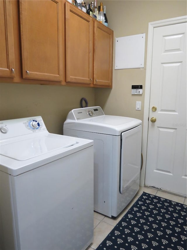 laundry room with washing machine and clothes dryer, light tile patterned floors, and cabinets