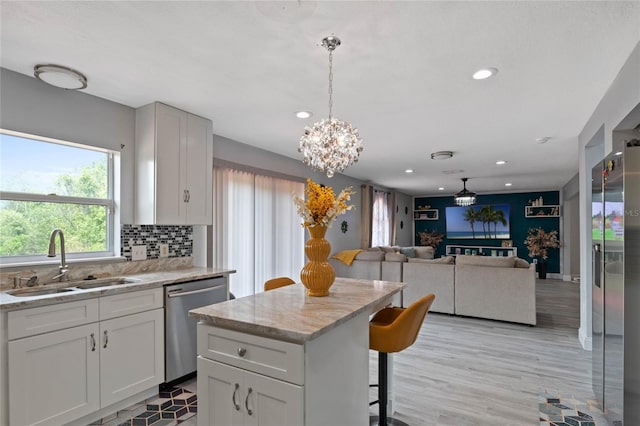 kitchen featuring light stone countertops, appliances with stainless steel finishes, sink, decorative light fixtures, and light hardwood / wood-style flooring