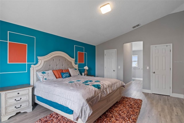 bedroom featuring a textured ceiling, light hardwood / wood-style flooring, and lofted ceiling