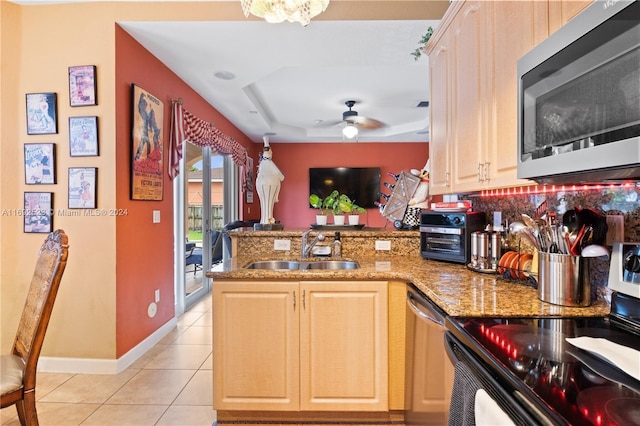 kitchen featuring a raised ceiling, stainless steel appliances, kitchen peninsula, light brown cabinetry, and sink